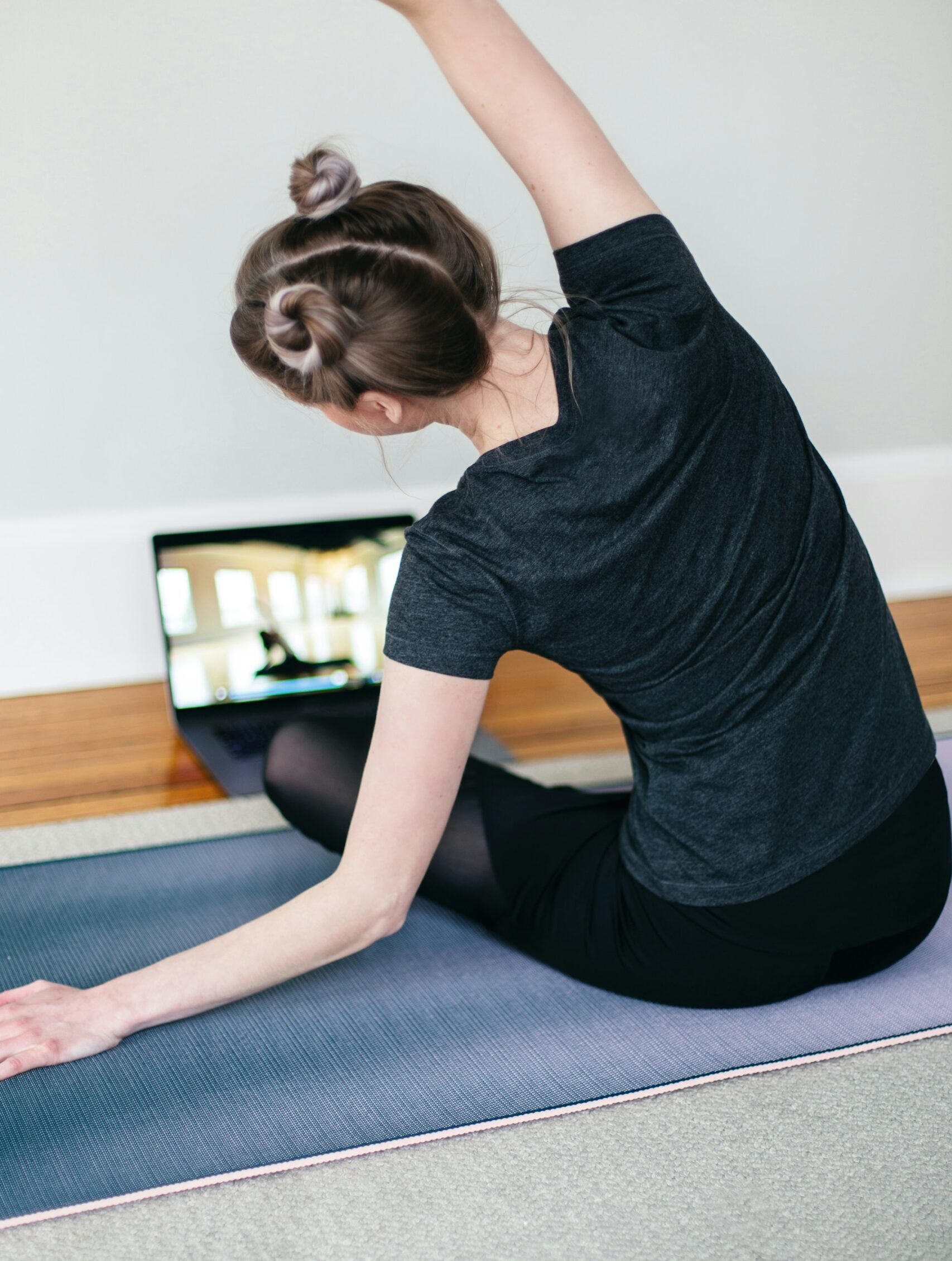 Woman stretching on a yoga mat with a laptop, preparing for ski season online.